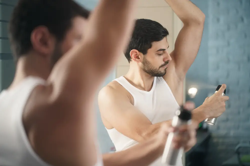 Young hispanic people and male beauty. Confident metrosexual man using spray deodorant on underarm skin, smiling and looking at mirror. beauty products that cause cancer 