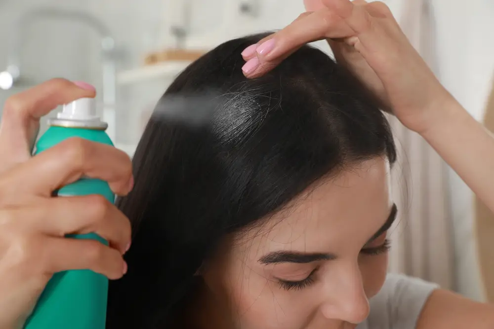 Woman applying dry shampoo onto her hair indoors, closeup. beauty products that cause cancer 